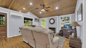 A cozy living room with a beige sectional sofa, a fireplace, a ceiling fan, and a television. - Charming 2-bedroom cabin in beautiful Mountain Rest on Lake Becky (Mountain Rest)