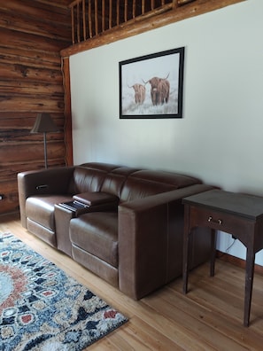 A brown leather sofa in a room with wooden walls and a framed picture of two yaks.
