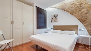 Une chambre à coucher comprenant un lit, une chaise, une table de chevet, une lampe fixée au mur et une grande fenêtre.