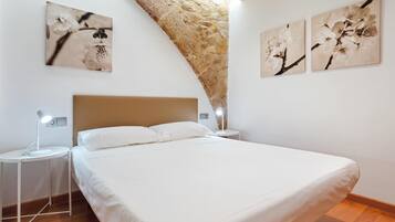Un dormitorio con una cama, dos mesitas de noche con lámparas y tres obras de arte colgadas en la pared que representan flores.