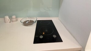 Une cuisine compacte avec une plaque de cuisson à induction noire, un saladier en verre et une pile de tasses blanches posées sur le comptoir.