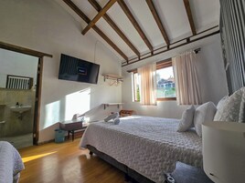 Un dormitorio con cama, escritorio, televisor, ventana con cortinas y vista a una casa exterior.