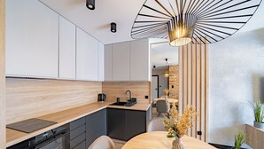A modern kitchen with a built-in oven, a dining area with a round table, and a unique pendant light fixture.