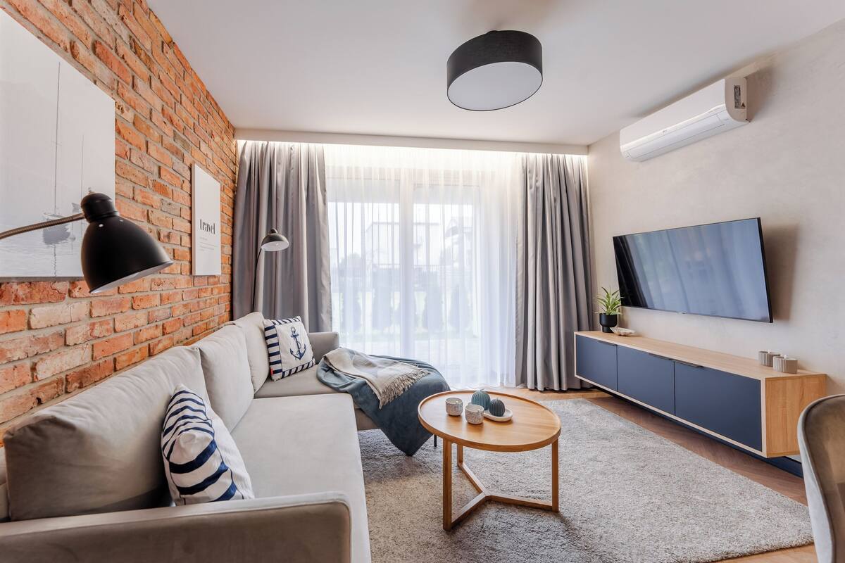 A modern living room with a brick wall, a sofa, a coffee table, a TV, and a large window with curtains.