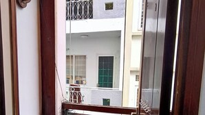 En smal balkon med gelænder i metal, et lille vindue og udsigt til omkringliggende bygninger.