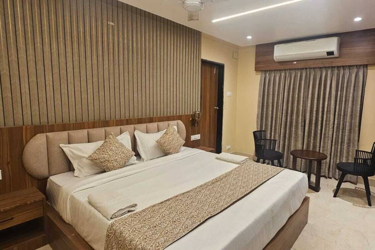 Habitación de hotel con una cama grande, una pequeña mesa con dos sillas, un equipo de aire acondicionado y un panel de pared de madera.