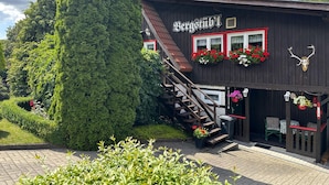 Un edificio tradicional con fachada de madera, una escalera que conduce a la entrada y macetas con flores en las ventanas.