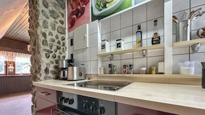 Una cocina con pared de piedra, horno empotrado, cafetera y diferentes especias en estantes.