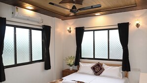 Ein Hotelzimmer mit Bett, Deckenventilator, Fenster mit Vorhängen, Wandklimaanlage und Nachttisch mit Lampe.