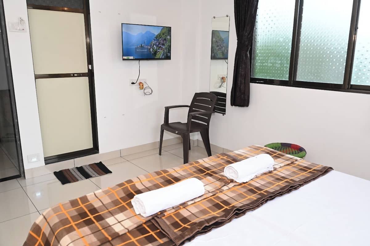 A hotel room with a bed, a chair, a television, and a window.