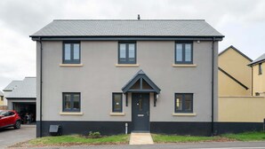 Ein zweistöckiges Wohngebäude mit grau-schwarzer Fassade, einem zentralen Eingang mit kleiner Veranda und zahlreichen Fenstern auf jeder Etage.