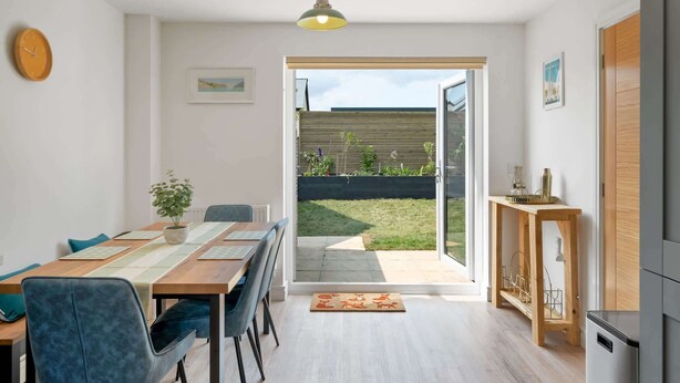 Eine moderne Küche mit Einbauofen, einem Holztisch mit Stühlen, einer Hängelampe und Blick auf den Garten durch die geöffnete Tür.