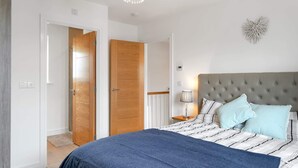 Ein Schlafzimmer mit einem großen Bett, einem gepolsterten Kopfteil, einer Nachttischlampe und einem Wanddekor.