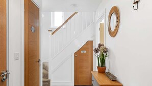 Ein Korridor mit einer Holztür, einer Treppe, einem Blumentopf und einem Spiegel an der Wand.