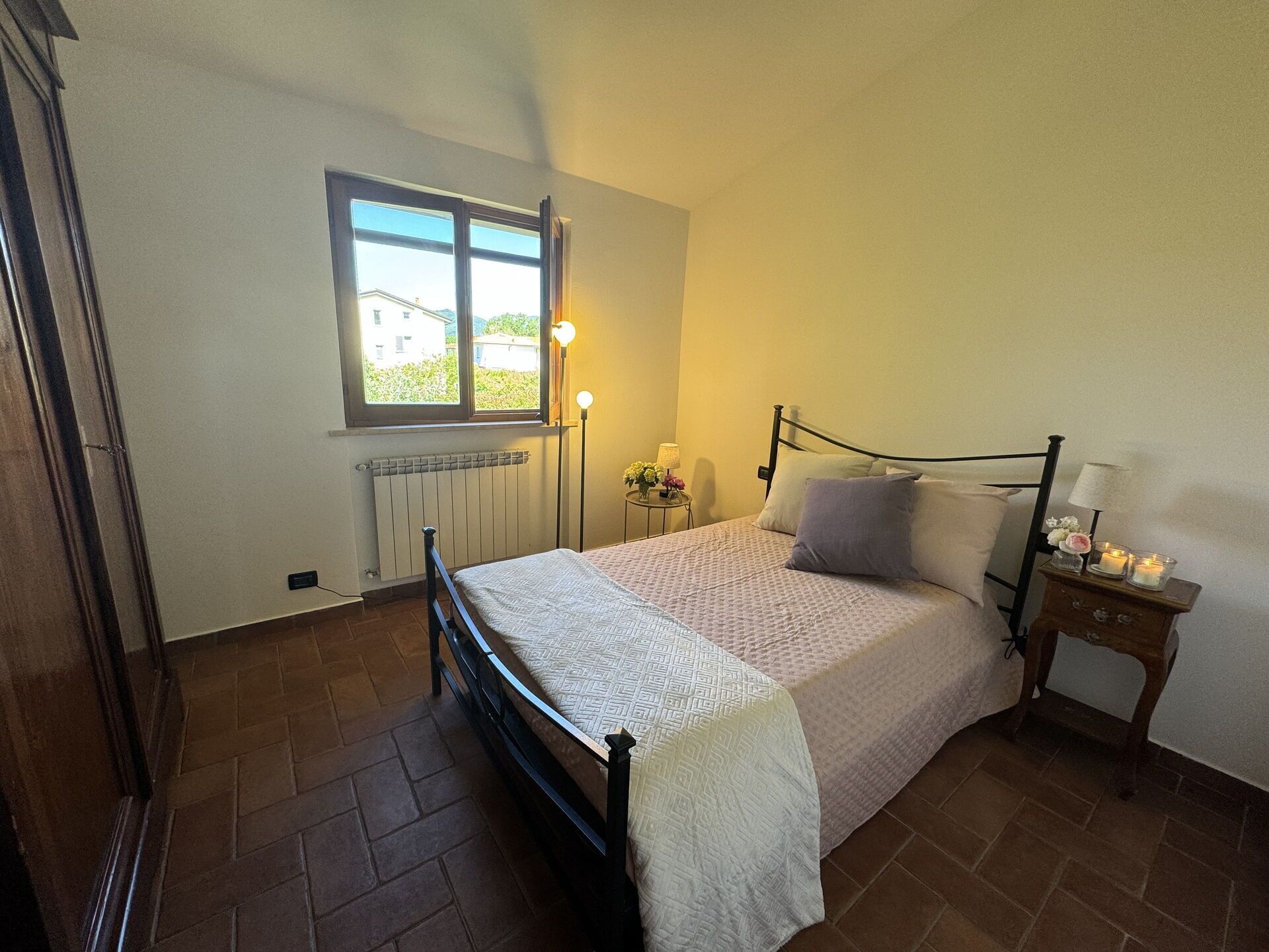 Una camera da letto con un letto, una finestra, un comodino con una lampada e un termosifone.