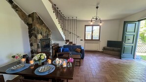 A dining area with a stone fireplace, a staircase, a blue sofa, and a dining table set with candles and flowers.