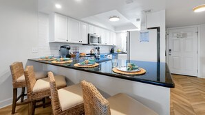 A modern kitchen with white cabinets, a central island with bar stools, and a refrigerator.