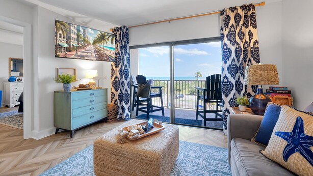 A living room with a sofa, a coffee table, and a view of the ocean through large windows.