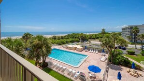 A pool area with a view of the beach, lounge chairs, and umbrellas.