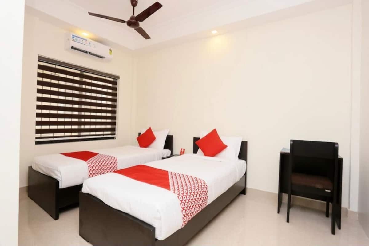 A hotel room with two beds, a ceiling fan, an air conditioning unit, and a single chair.