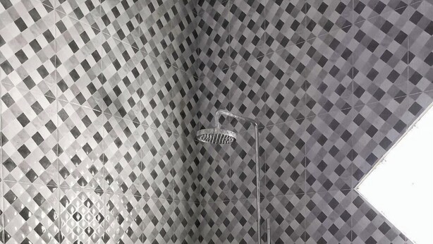 Ein Badezimmer mit Wandfliesen in Rautenmuster, einer Dusche inklusive Handbrause und einem kleinen Fenster.