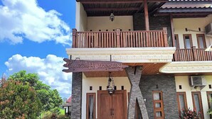 Ein zweistöckiges Gebäude mit Balkon und einer Steinfassade, auf der ein Schild mit der Aufschrift 'Senada Homestay' zu sehen ist.