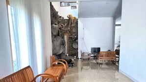 A spacious living area with a long wooden bench, a stone wall, and a television. - Benada Piyungan Yogyakarta by ABM (Berbah)