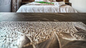Un dormitorio con techo de madera, una cama con ropa de cama blanca, una mesita de noche con lámpara y una ventana con cortinas.