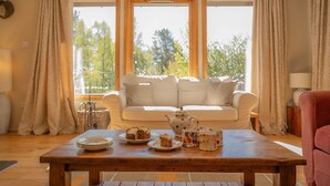 Un salón acogedor con una mesa de madera, un sofá blanco y vistas amplias a través de grandes ventanales.