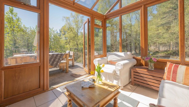 Una habitación iluminada por el sol, con piso de madera, un sofá, una mesa de centro y vistas a una terraza y árboles.