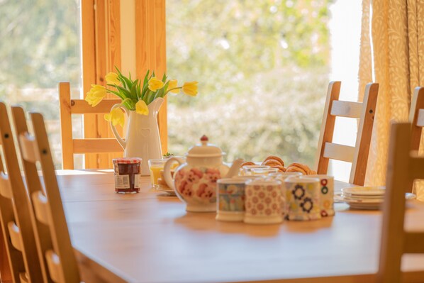 A wooden table with a vase of yellow flowers, a teapot, and patterned cups.