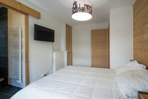A bedroom with a large bed, a mounted TV, a radiator, and wooden paneling on the walls.