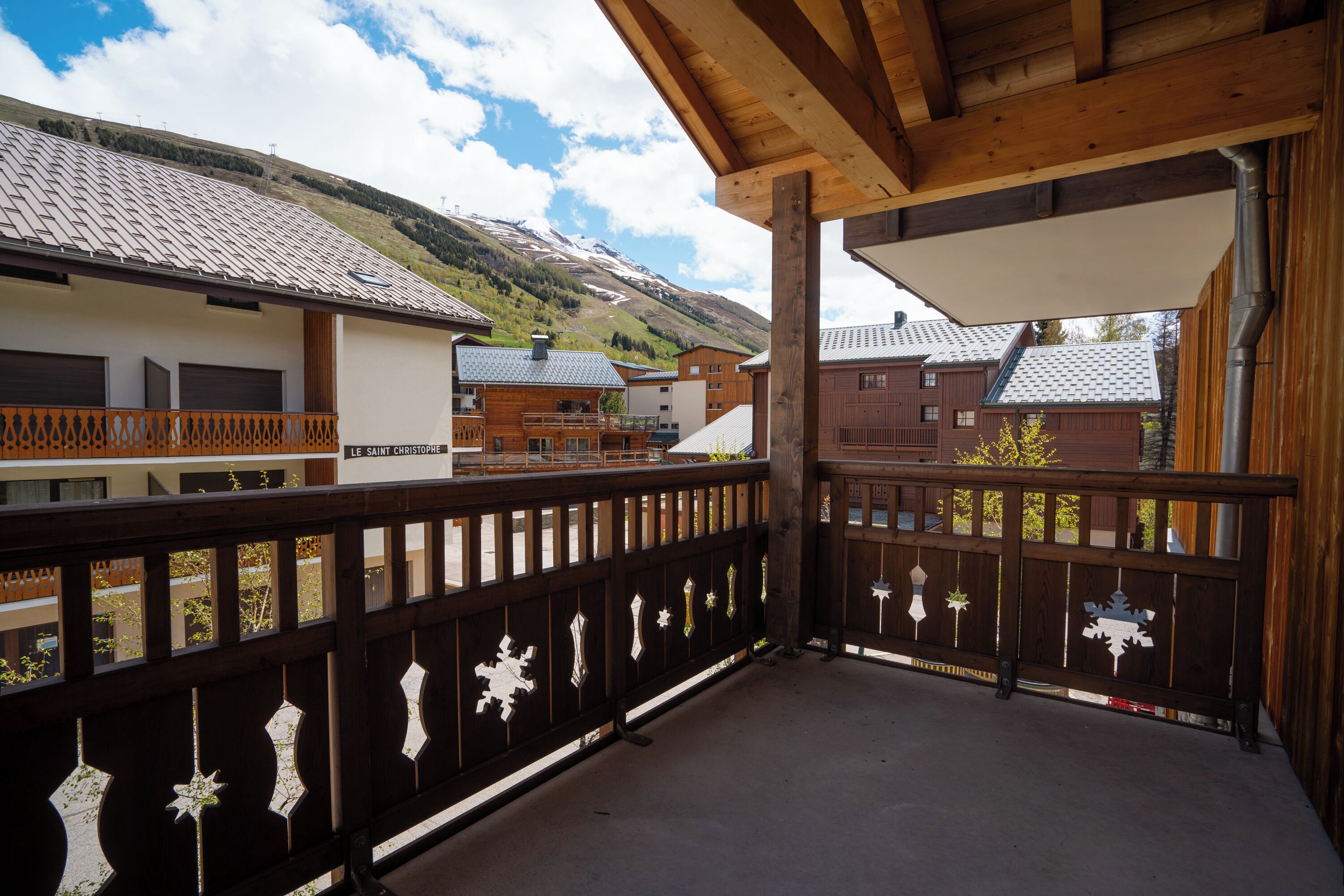 A wooden balcony with snowflake decorations, overlooking a mountainous area with buildings.