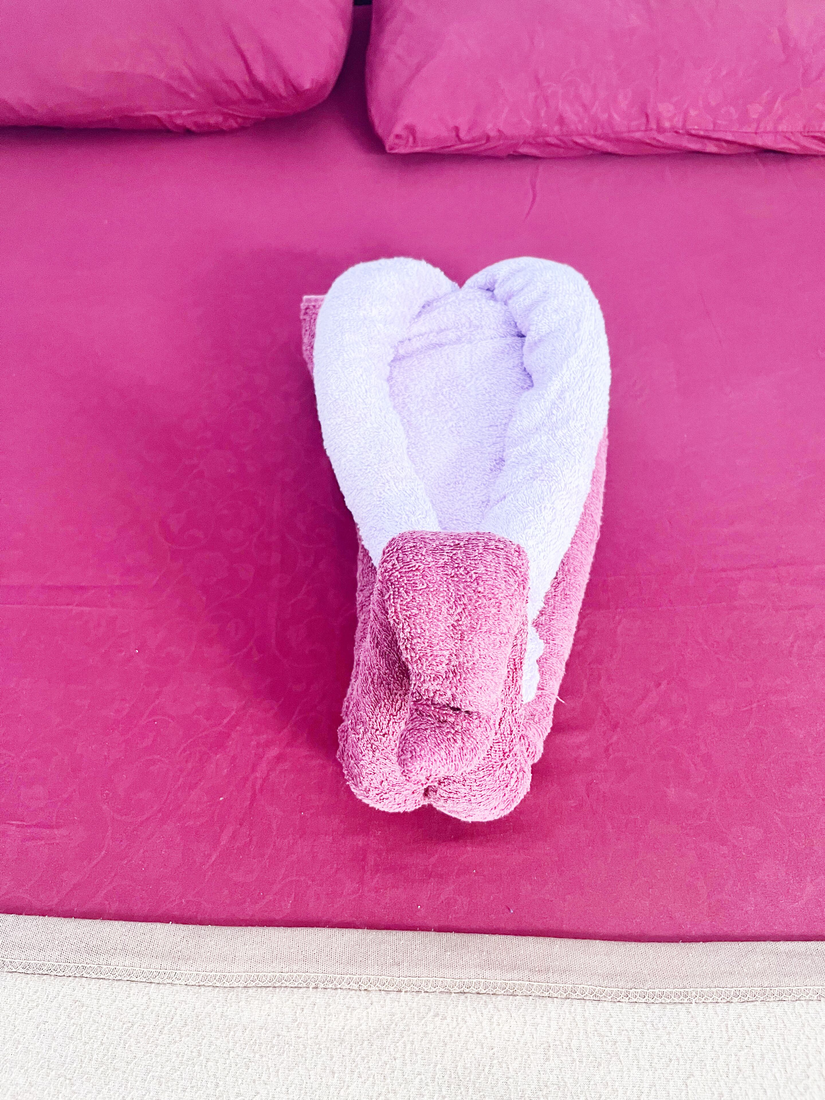 Una toalla doblada con cuidado sobre una cama con cubrecolcha rosa.