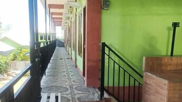 A corridor with a tiled floor, a wooden bench, and a green wall with a black railing. - ZELLA KOST & HOMESTAY (Labuan Bajo)