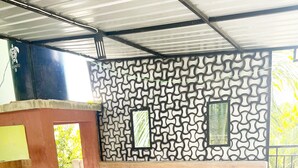 A covered outdoor area with a long white table, a patterned wall, and a metal roof structure. - ZELLA KOST & HOMESTAY (Labuan Bajo)