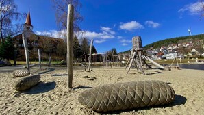 A playground with sand, wooden structures, and a church in the background. - NEW: Exclusive Waldliebe apartment with indoor pool and sauna (Schonach im Schwarzwald)