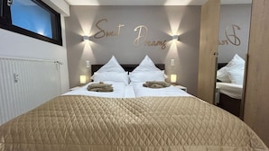 A neatly made bed with a quilted beige cover, two bedside lamps, and a wall with the words "Sweet Dreams" illuminated. - NEW: Exclusive Waldliebe apartment with indoor pool and sauna (Schonach im Schwarzwald)