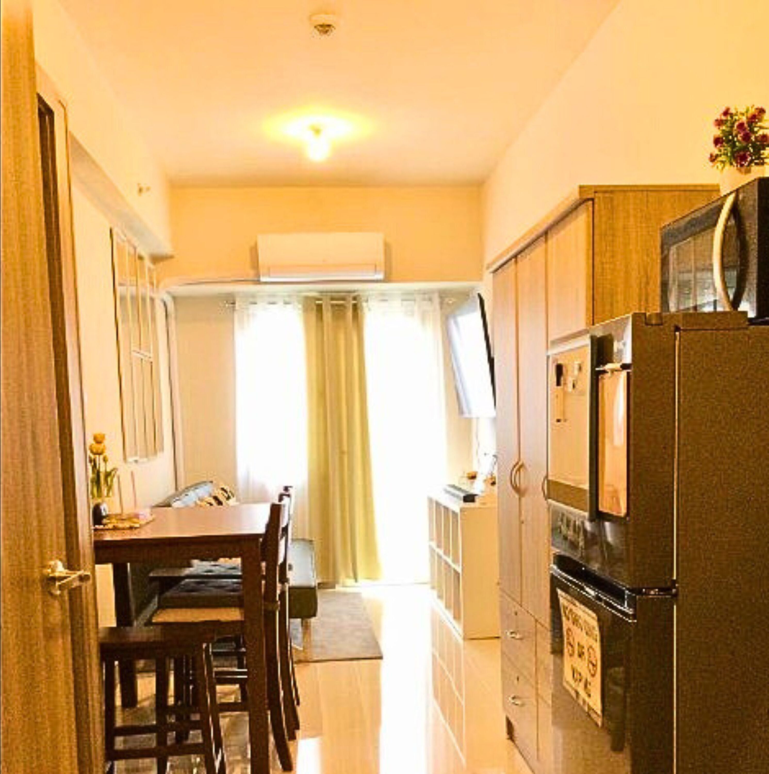 Una cocina compacta con refrigerador, una mesa de comedor con sillas y una ventana con cortinas.