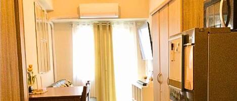 Una cocina compacta con refrigerador, una mesa de comedor con sillas y una ventana con cortinas.