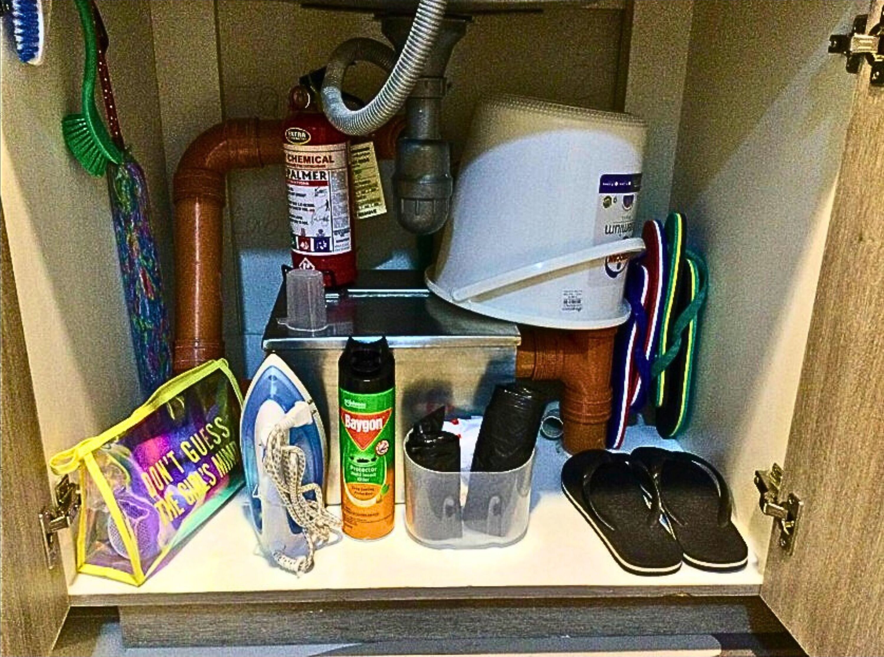 A bathroom sink area with a toothbrush, a fire extinguisher, a hairdryer, a plastic container, and a pair of shoes.