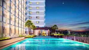 A modern hotel with a rooftop pool, a covered seating area, and a city skyline view at dusk. - Rent Xpress Online US Embassy (Pasay)