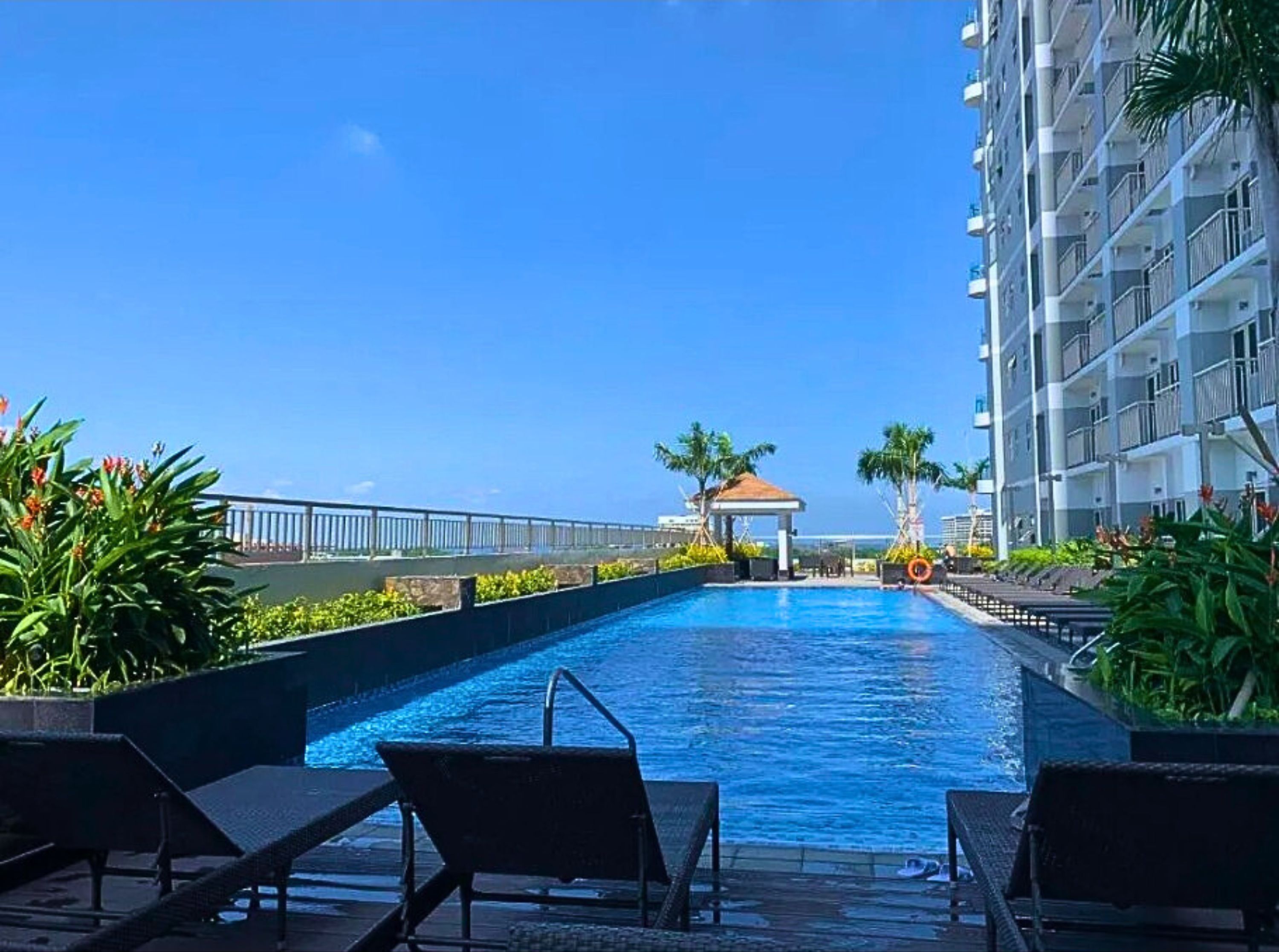 Una piscina con sillas de descanso, un pabellón y vistas a un edificio alto.