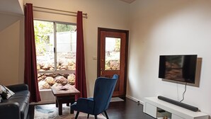 A living room with a dark wood floor, a blue chair, a sofa, a TV on a white stand, and a window with curtains. - Peaceful relaxing Getaway in Karri Forest bordering a Nature Reserve. (Kentdale)