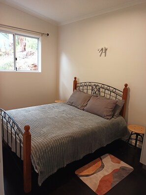 A bed with a metal frame and wooden headboard, a grey blanket, and a small round stool beside it. - Peaceful relaxing Getaway in Karri Forest bordering a Nature Reserve. (Kentdale)