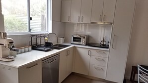 A modern kitchen with white cabinets, a built-in dishwasher, a coffee machine, and a microwave. - Peaceful relaxing Getaway in Karri Forest bordering a Nature Reserve. (Kentdale)