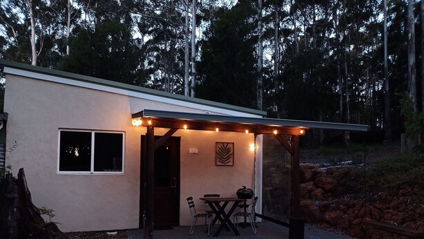 A covered patio area with a table and chairs, a small window, and a decorative leaf wall art piece. - Peaceful relaxing Getaway in Karri Forest bordering a Nature Reserve. (Kentdale)