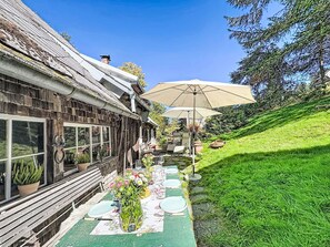A rustic outdoor seating area with a table set for dining, a large umbrella, and a grassy slope. - Winterberg by Interhome (Feldberg)