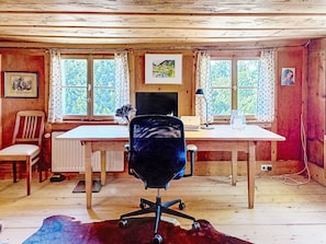 A rustic cabin interior with a wooden desk, a black office chair, a radiator, and a window with curtains. - Winterberg by Interhome (Feldberg)