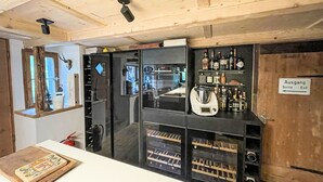 A bar area with a wooden ceiling, a black refrigerator, shelves with bottles, and a sign indicating an exit. - Winterberg by Interhome (Feldberg)